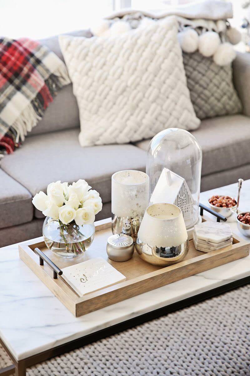 تزیین میز جلو مبلی سنگی با سینی چوبی که درون آن شمع و گل های سفید قرار داده شده است تا سطح را مرتب نگه دارد